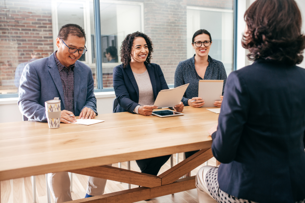 3 people holding papers interviewing a person across the desk to accompany What Not to Do at an Interview blog post